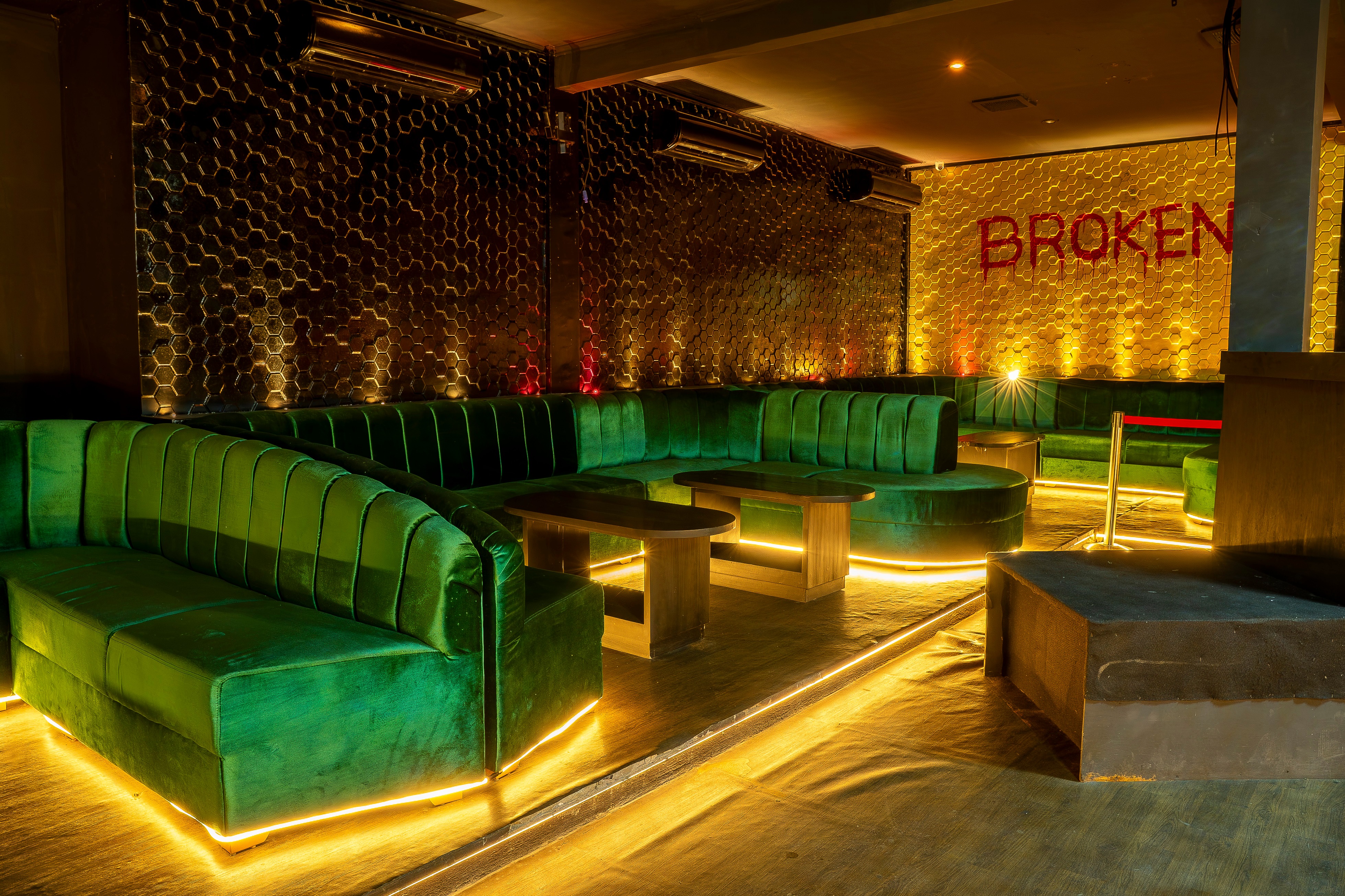 Green velvet seating with BROKEN neon sign on honeycomb wall