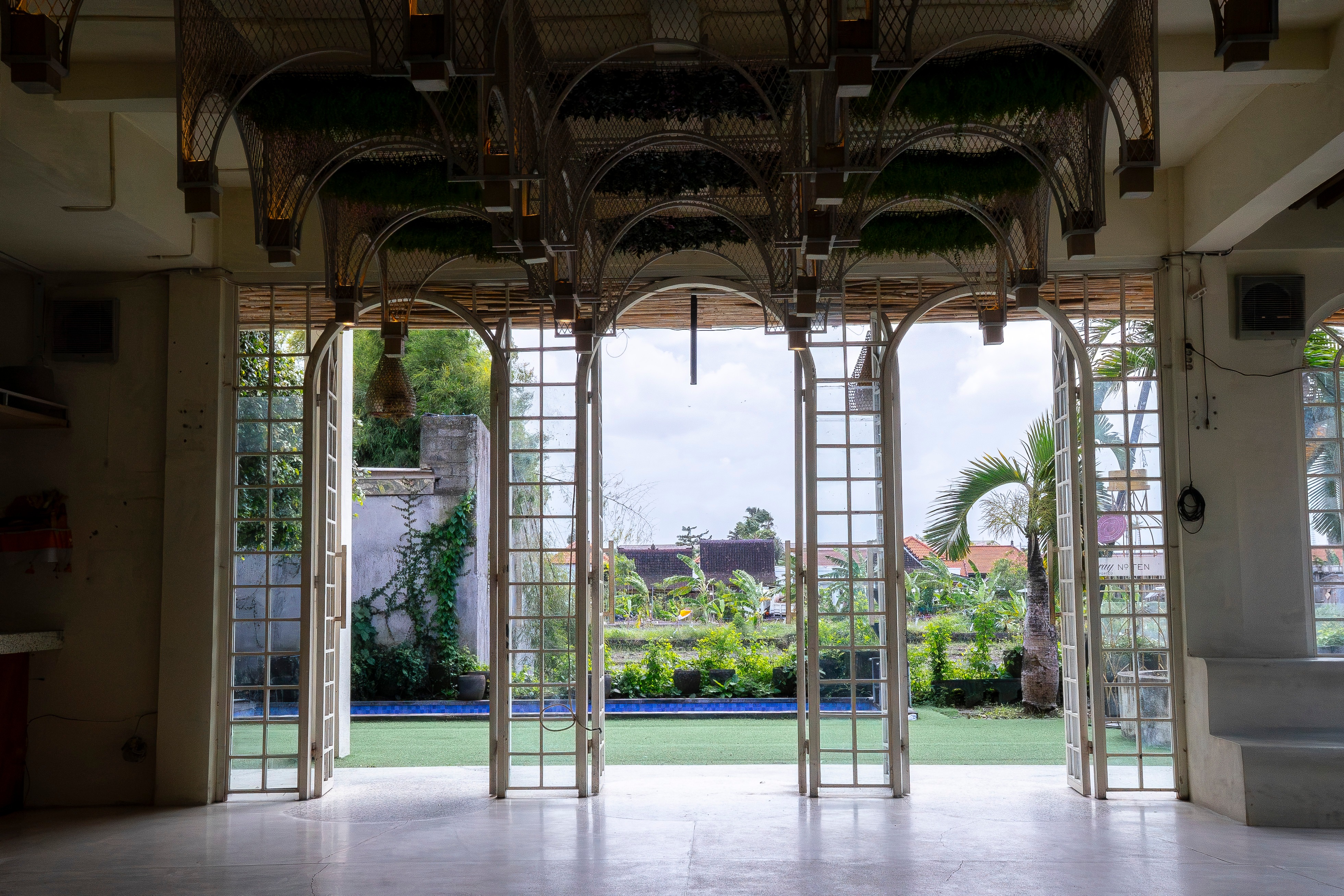 Interior view through elegant arched glass doors with wicker ceiling details and garden pool view